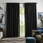 Full-length black rod pocket blackout curtains drawn open to reveal a window