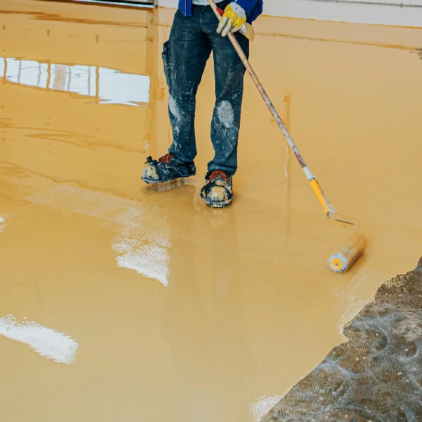 Worker applying yellow epoxy floor coating with roller