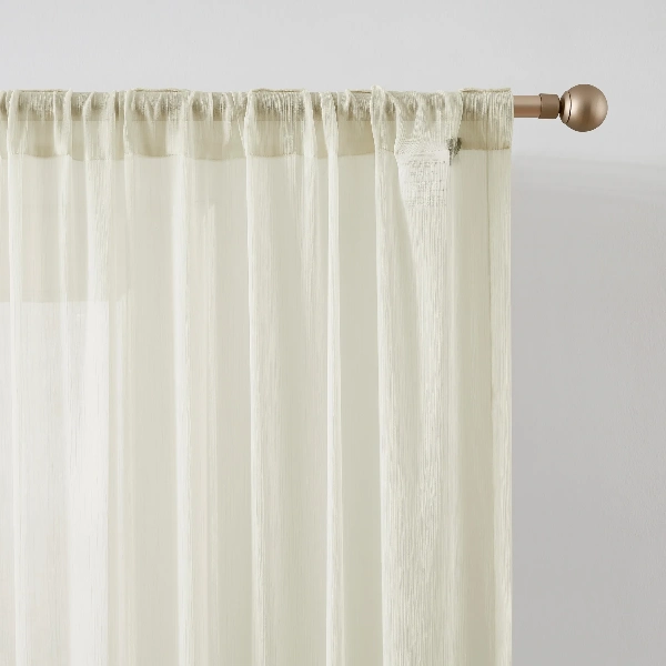 off-white sheer curtain in rod pocket heading style.