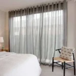 A light gray sheer curtain covering a large window in a modern bedroom.