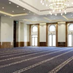 blue mosque carpet with gold and white striped prayer lines covering a large hall