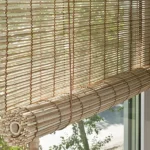 light-colored woven bamboo roll-up blind, showing the rolled bottom edge